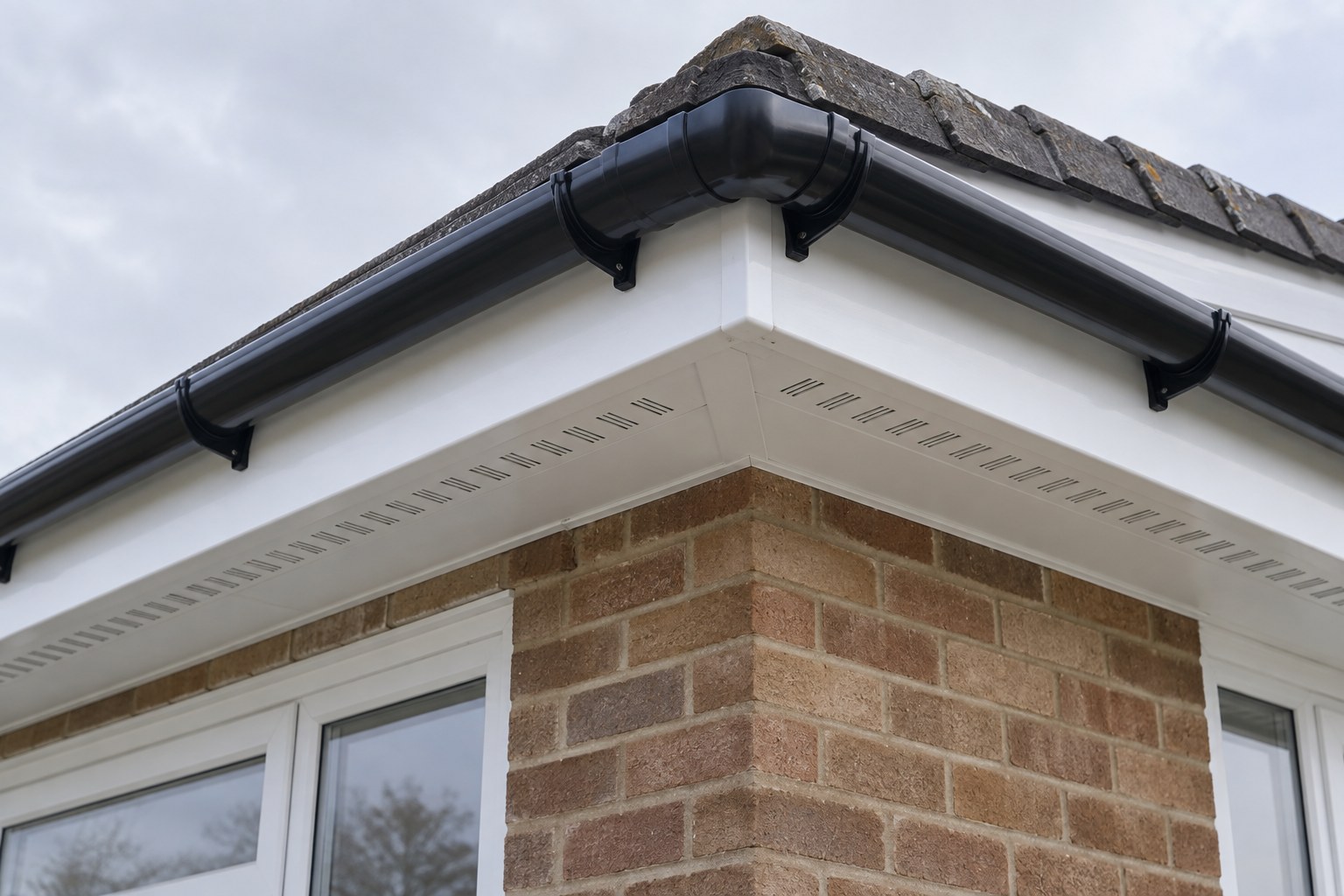 New white fascia and vented soffit beneath black guttering at a tiled roof corner